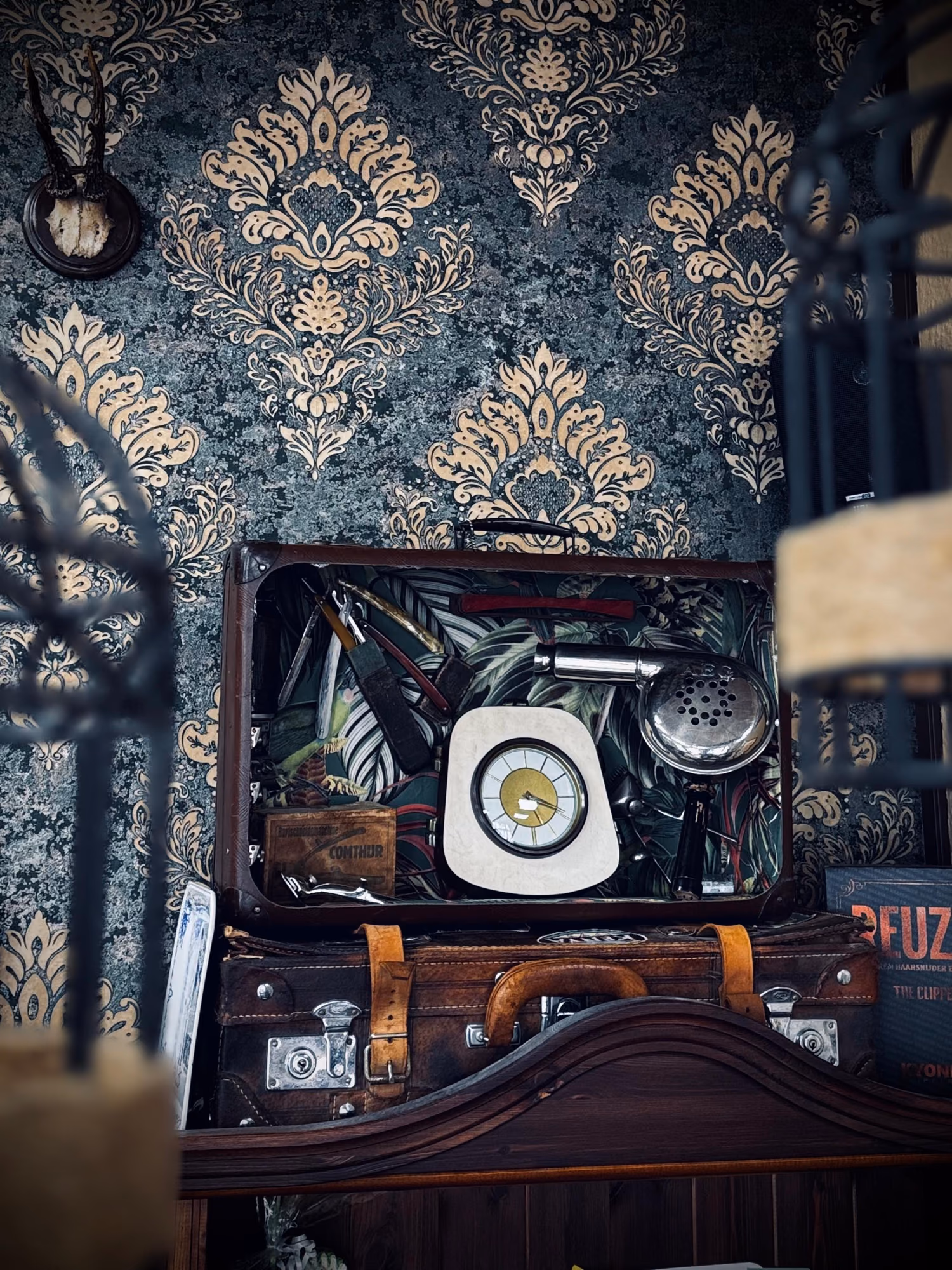 Vintage-Koffer mit altem Barbierwerkzeug vor Damasttapete